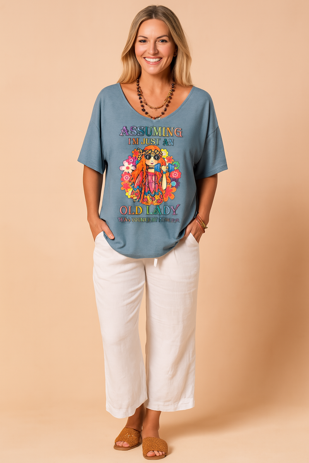 Blauwgrijs dames-T-shirt met diepe V-hals en kleurrijke hippieprint inclusief bloemen en tekst “Assuming I’m just an old lady”, gemaakt van luchtige, soepele stof voor een relaxte zomerse pasvorm.