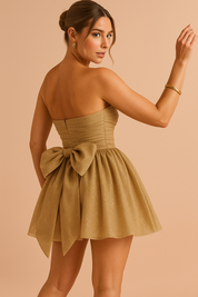 Vrouw draagt gouden strapless glitter mini jurk met grote strik, achteraanzicht
