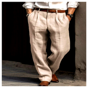 Beige linnen herenbroek met plooien en rechte pijpen, casual gestyled met bruine riem en leren schoenen voor een luchtige, verzorgde uitstraling.