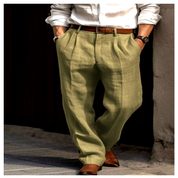 Licht olijfgroene linnen herenbroek met plooien en rechte pasvorm, gestyled met bruine riem en nette schoenen—perfect voor zomerse elegantie.