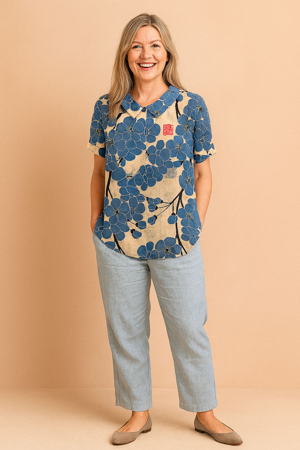 Beige linnen blouse met korte mouwen, opvallend grote blauwe bloemen en zwarte takken in een artistieke all-over print, voorzien van rood vierkant detail op de borst.