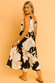 Mouwloze midi-jurk met zwarte en caramelkleurige oversized bloemenprint op een crèmekleurige achtergrond, afgewerkt met ruches in lagen.