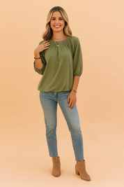 Olijfgroene dames top met ronde hals en driekwartmouwen, uitgevoerd in een zachte jersey stof. Voorzien van elegante plooien rond de halslijn en elastische mouwboorden voor een subtiele pofmouw. De losvallende pasvorm biedt zowel comfort als een vrouwelijke uitstraling.