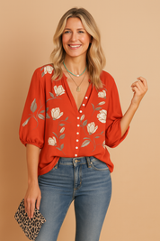 Felrode blouse met knoopsluiting, witte tulpenmotieven en geplooide 3/4-mouwen, gecombineerd met een lichte spijkerbroek.