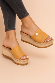 Sleehak sandaal met gevlochten platformzool en brede instapband met goudkleurig decoratief detail, perfect voor zonnige dagen en vakantie-outfits.