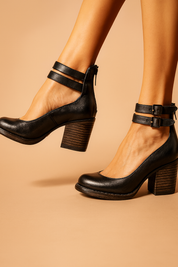 Zwarte pump met leren look, blokhak, ronde neus, dubbele enkelbandjes met gespen en ritssluiting achteraan.